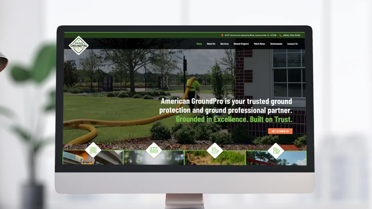 A computer monitor displays the American GroundPro website homepage, showing a worker on a green lawn near landscaping, with text promoting ground protection and professionalism.