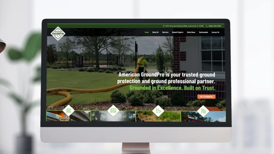A computer monitor displays the American GroundPro website homepage, showing a worker on a green lawn near landscaping, with text promoting ground protection and professionalism.